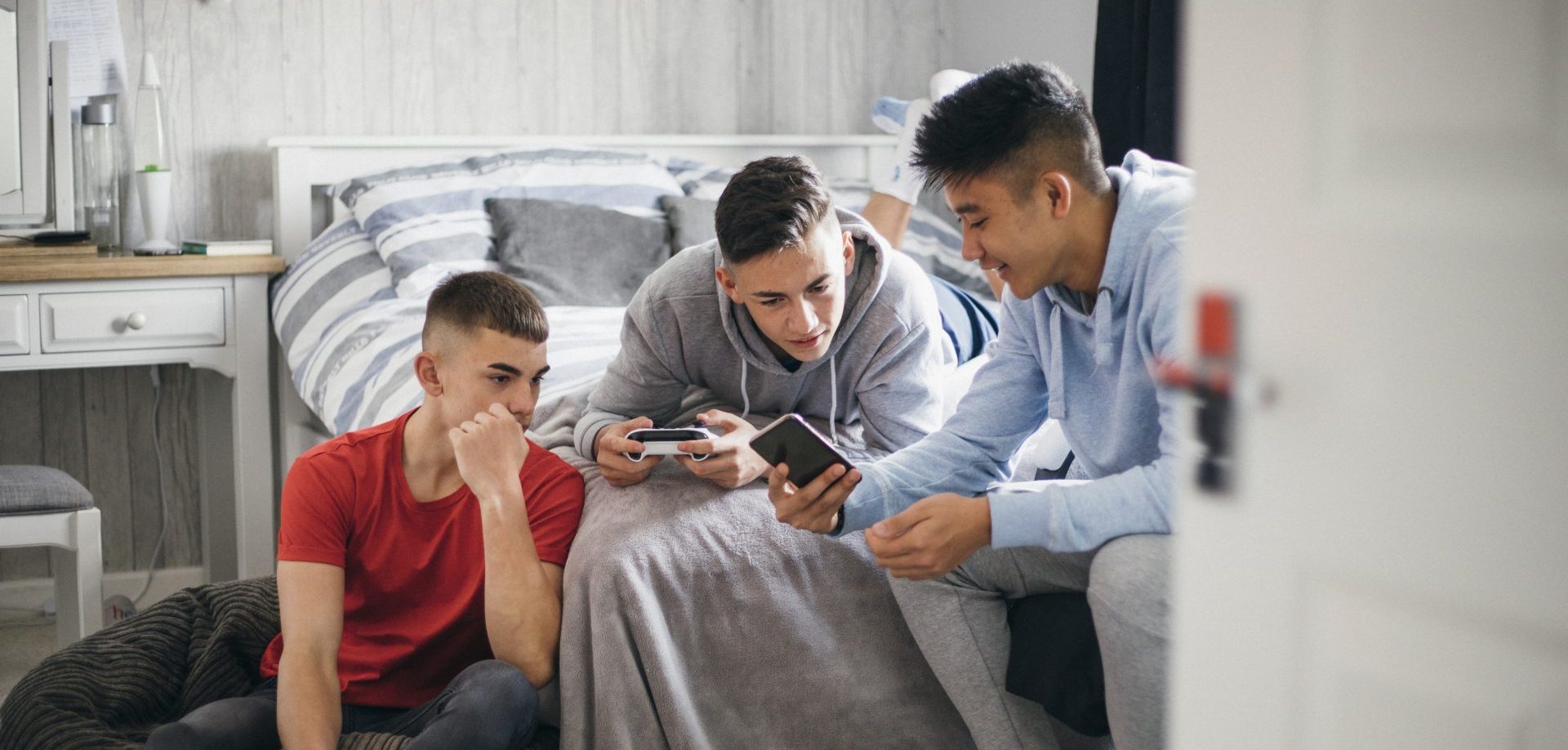 Three teenage boys looking at their mobile phones and chatting.
