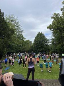 the photo shows hundreds of people in a park who are participating in a group exercise class